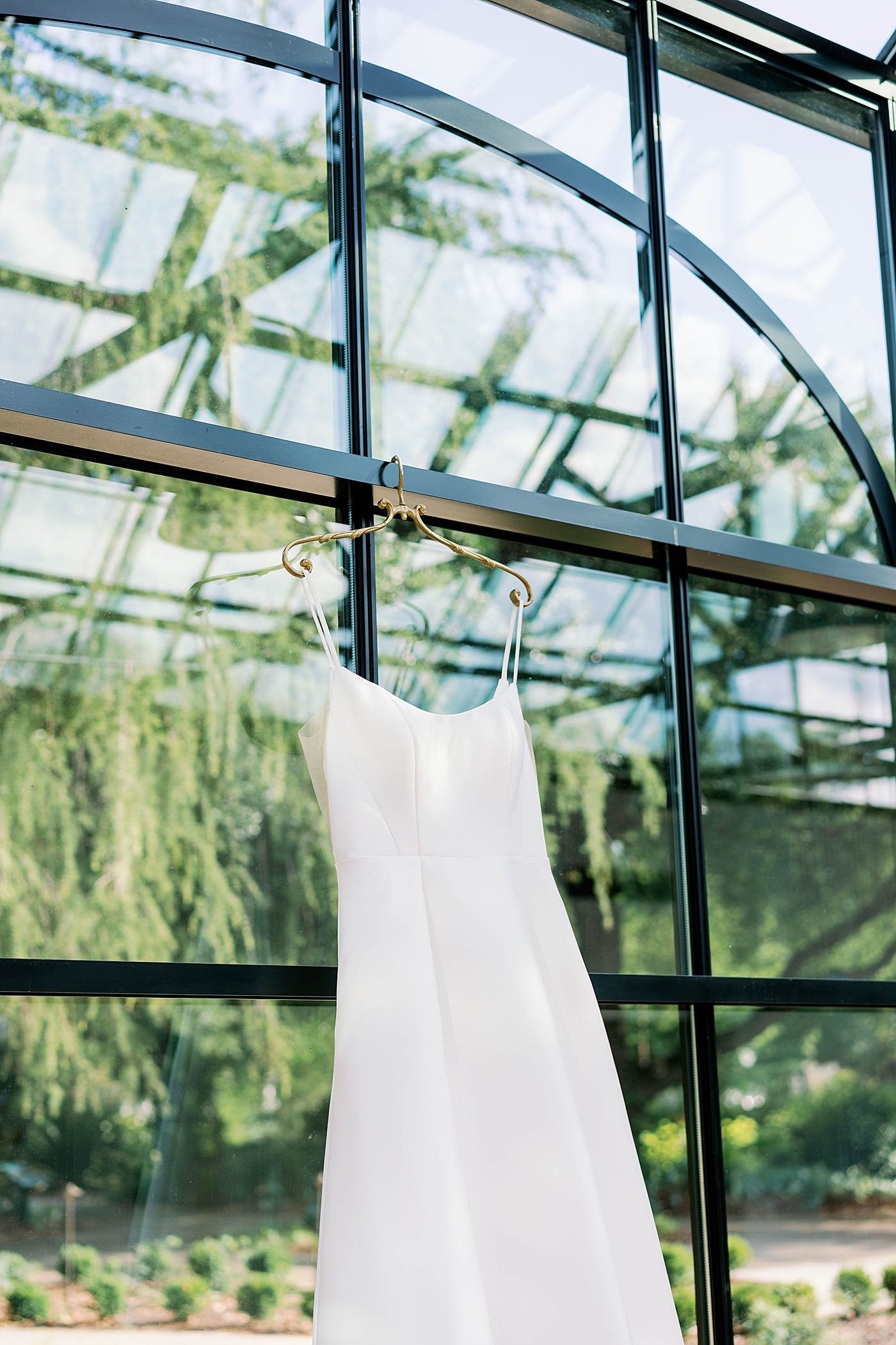 Bridal gown hanging on a gold hanger in a greenhouse | Photo by Annie Laura Photo