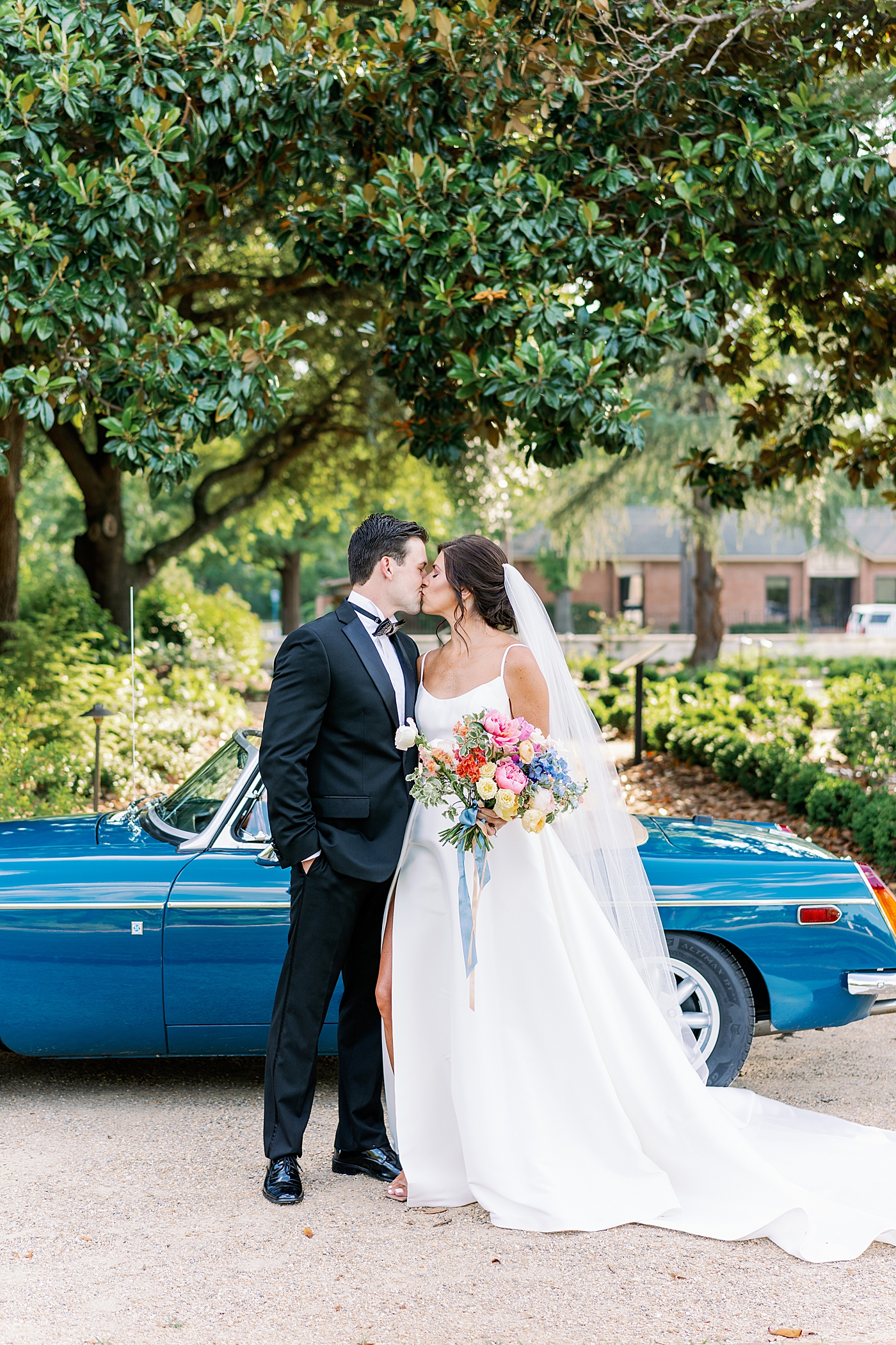 Bride and groom kissing by vintage car at Boyd Foundation Horticultural Center | Photo by Annie Laura Photo