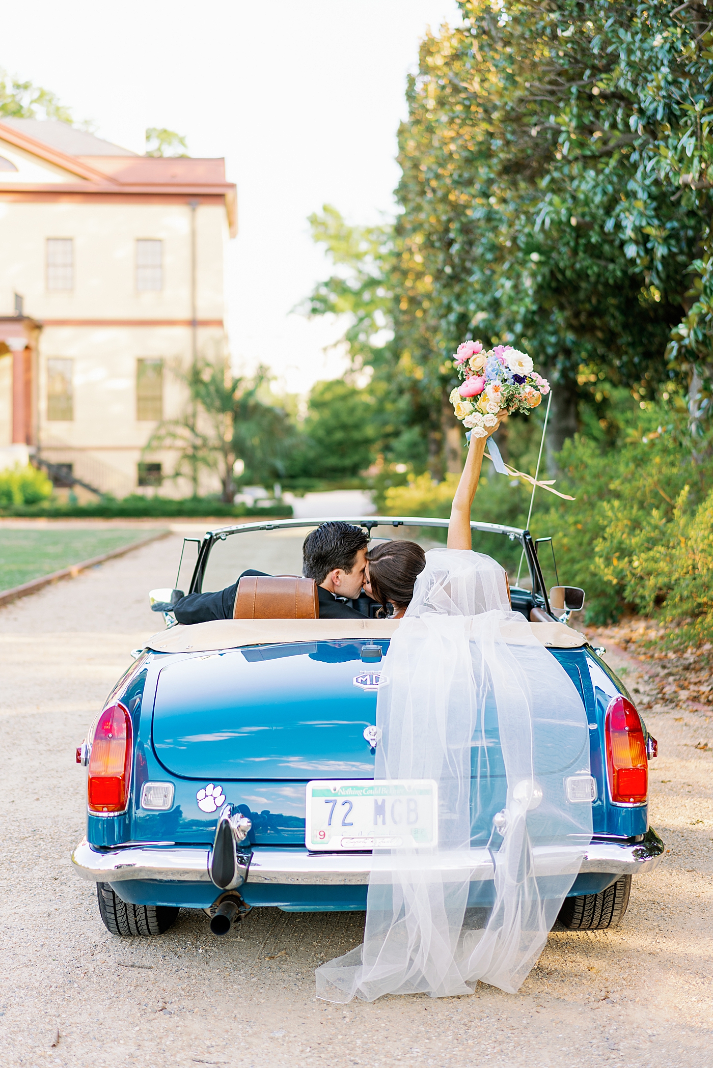 Bride and groom kissing in a blue convertible while she holds up her bouquet | Photo by Annie Laura Photo