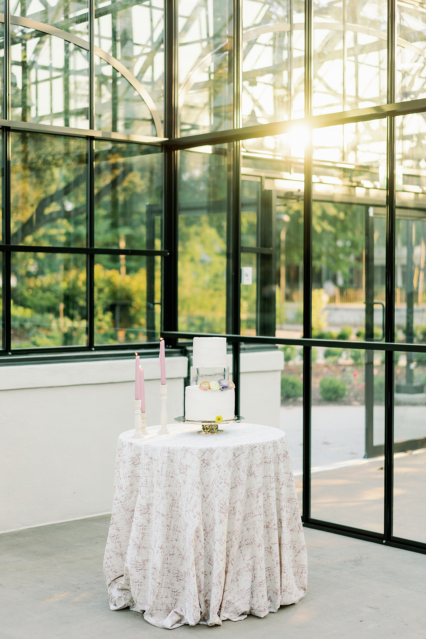 Cake table with cake and pink pillar candles in a greenhouse | Photo by Annie Laura Photo