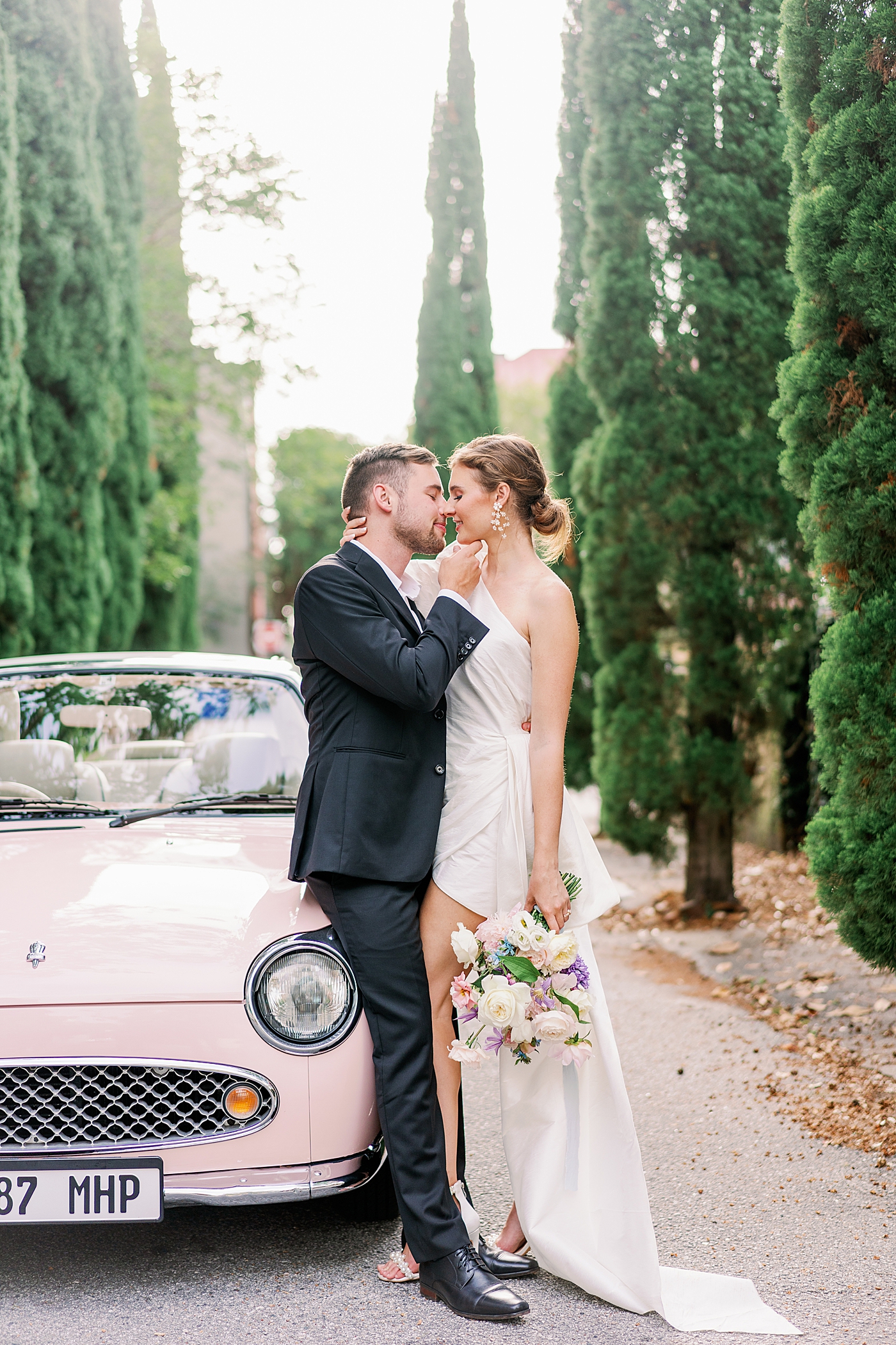 Bride and groom kissing near pink car during Elevated City Hall Elopement | Images by Annie Laura Photo