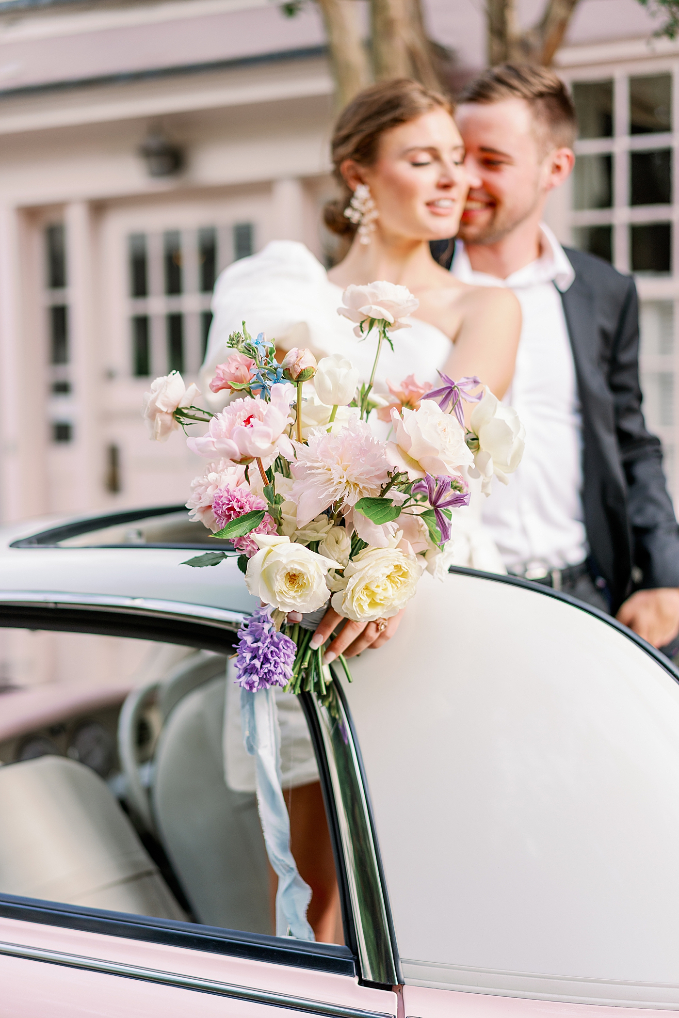 Detail of pastel bouquet held by bride snuggled by groom in pink convertible | Images by Annie Laura Photo