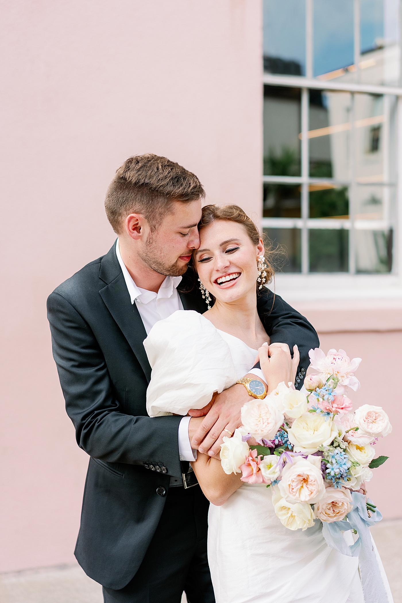 Bride and groom snuggling in front of pink wall during Elevated City Hall Elopement in Charleston | Images by Annie Laura Photo