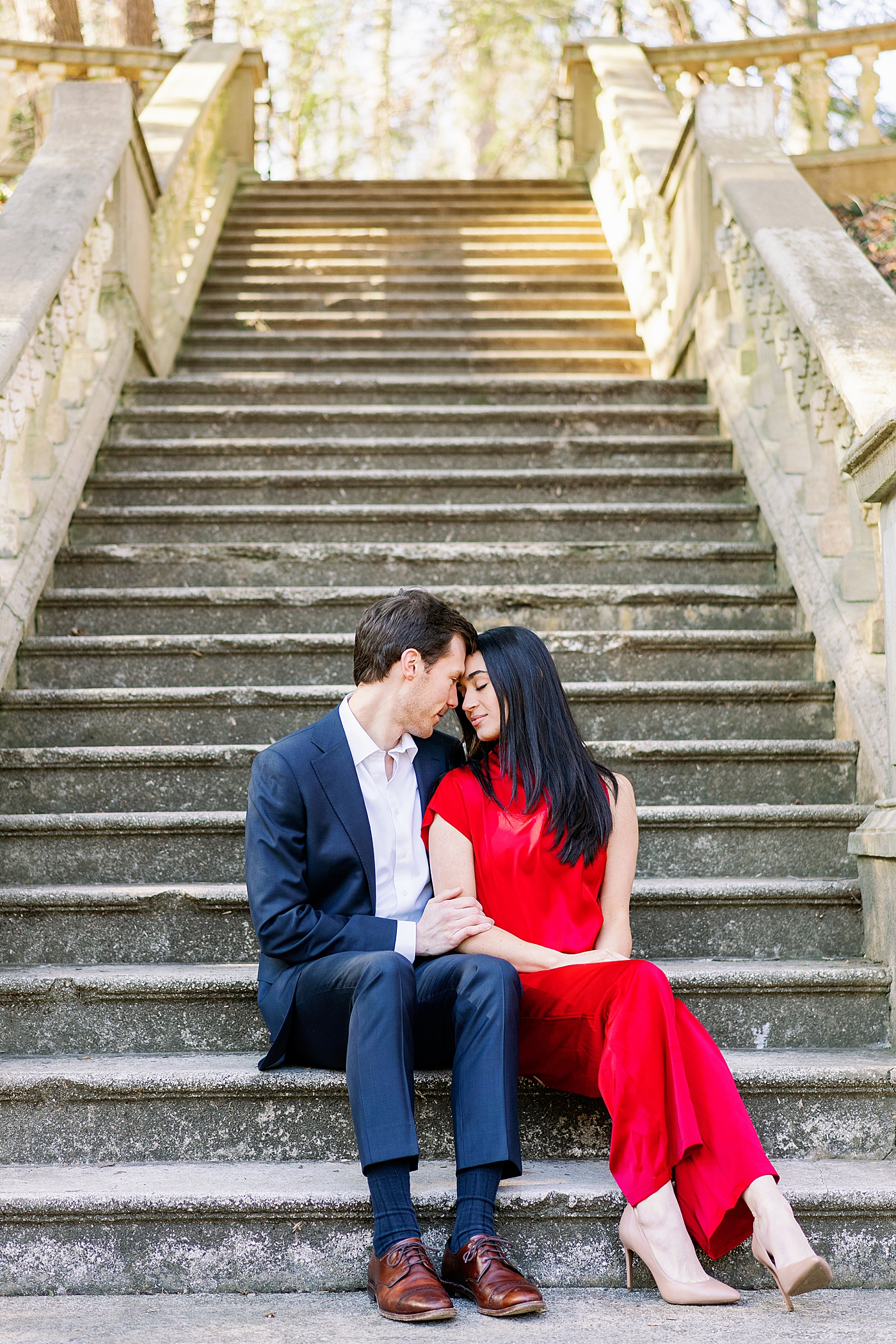 Couple in red and blue embracing sitting on stone staircase during their Atlanta, GA Garden Engagement | Image by Annie Laura Photo