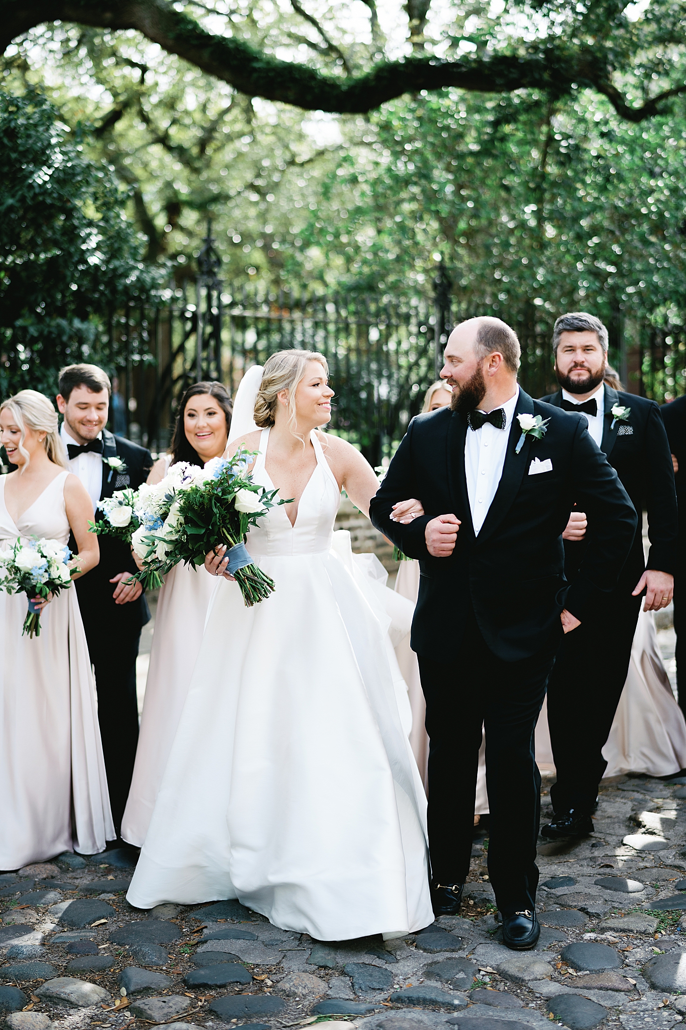 Bride and groom walking on a cobblestone street with their wedding party | Image by Annie Laura Photo