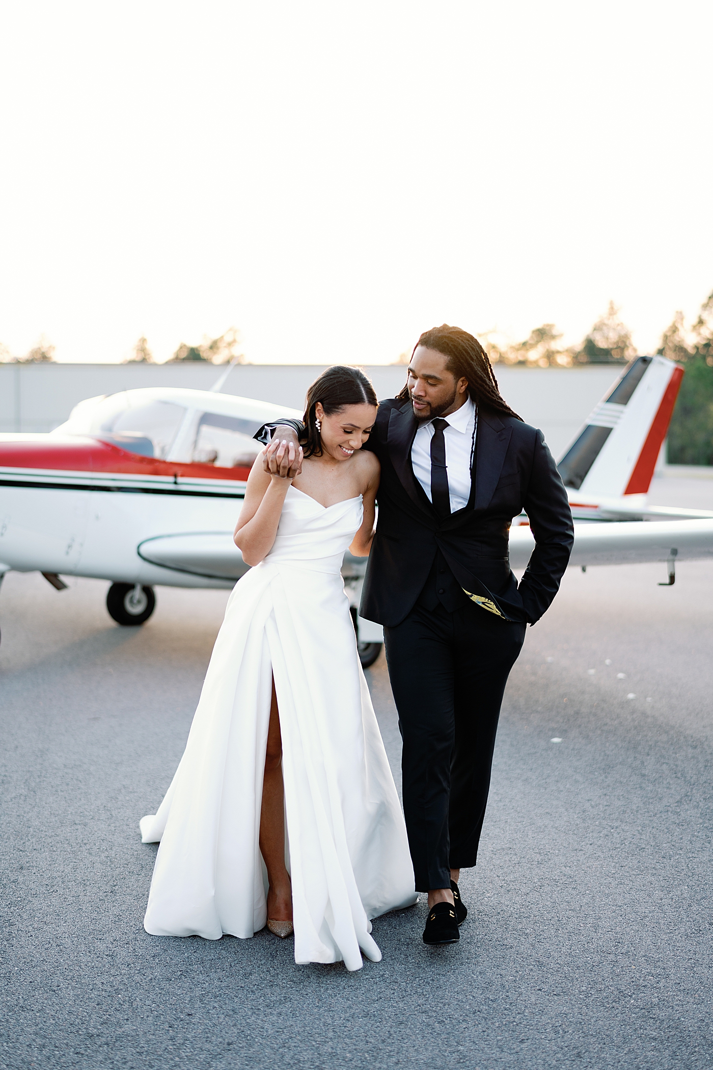 Bride and groom walking with an airplane in the background | Image by Annie Laura Photo
